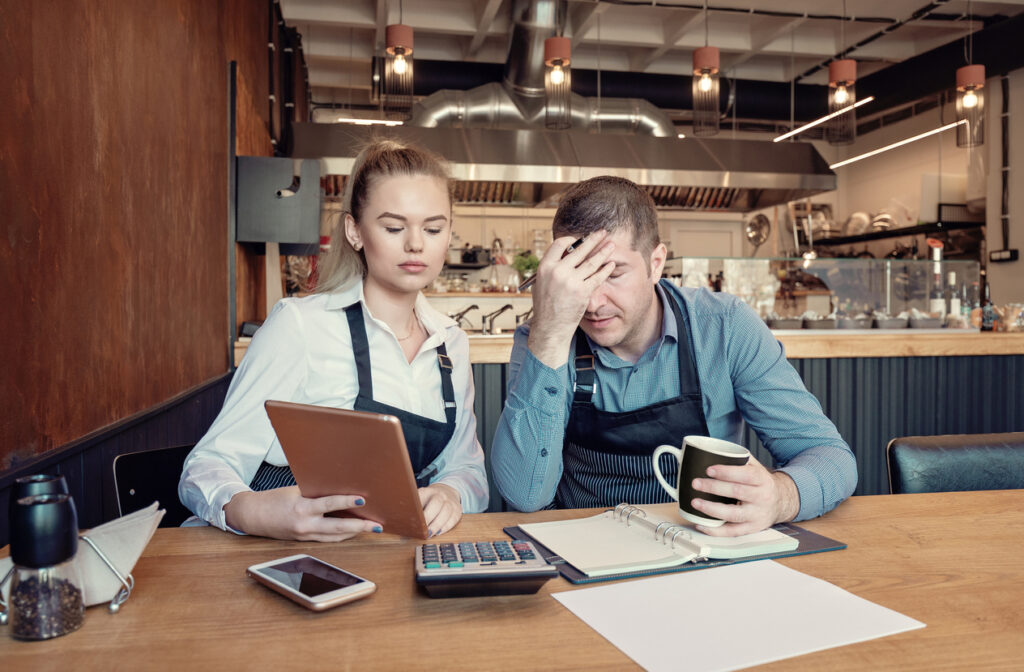 A worried manager and employee at a coffee shop looking at the reports realising they have lost some customers and profits