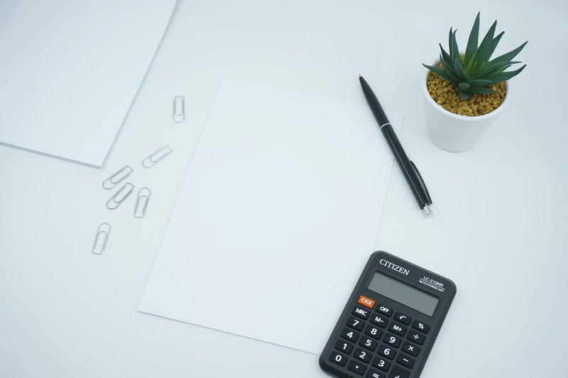 a desk with paper, pen, fake plant and calculator. when setting up a dog walking business, you need to work out your prices